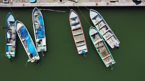 Vista-Aérea-Mirando-Directamente-Hacia-Abajo-Y-La-Cámara-Deslizándose-Hacia-La-Derecha-Mostrando-Pequeños-Barcos-Pesqueros-De-Madera-En-Un-Puerto-En-México