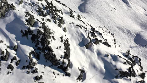 Un-Dron-Disparó-Hacia-Adelante-Sobre-La-Roca-Y-La-Ladera-De-La-Montaña-Cubierta-De-Nieve,-Antes-De-Inclinarse-Hacia-Arriba-Para-Revelar-La-Montaña-Y-Las-Pistas-De-Esquí-Fuera-De-Pista-En-La-Nieve