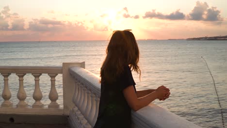 woman watching sunset over the ocean from a balcony