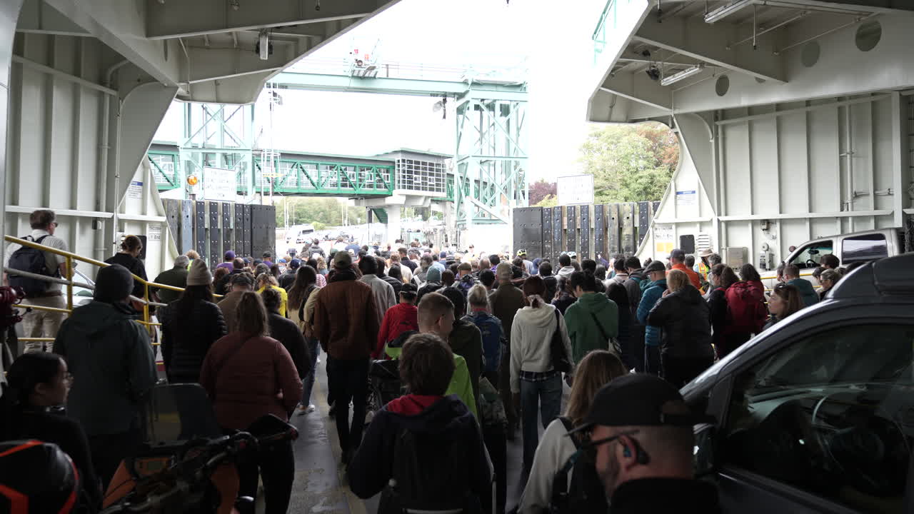 Large crowd of people walking off a ferry at Bainbridge Island, heading towards the exit on a cloudy day.