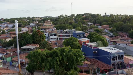 Dolly-out-aerial-drone-shot-flying-away-from-the-colorful-beach-homes-and-restaurants-of-the-famous-tourist-town-of-Pipa,-Brazil-in-Rio-Grande-do-Norte-on-a-warm-sunny-summer-day