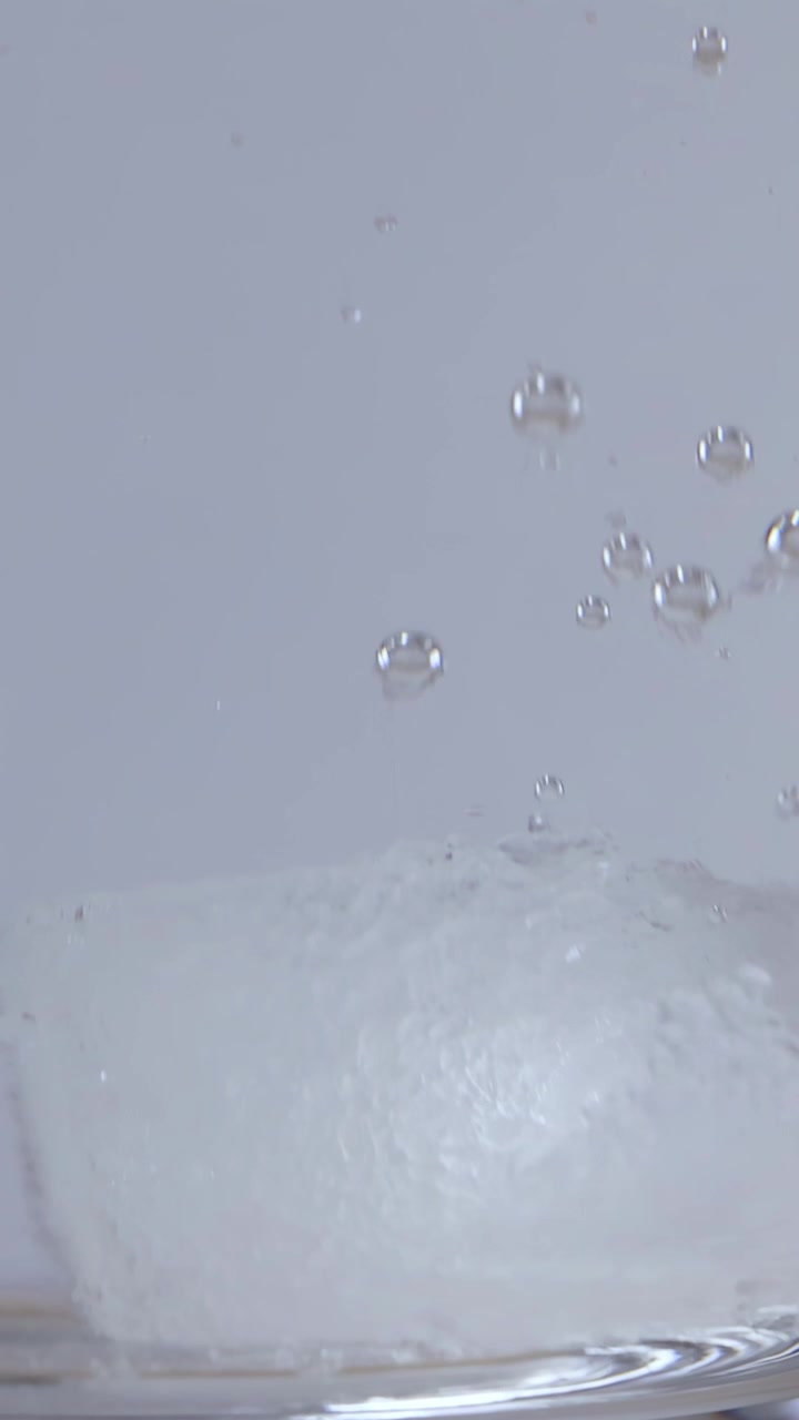 Primo piano di cristalli di zucchero bianco che si dissolvono in acqua calda con bolle che salgono in una tazza