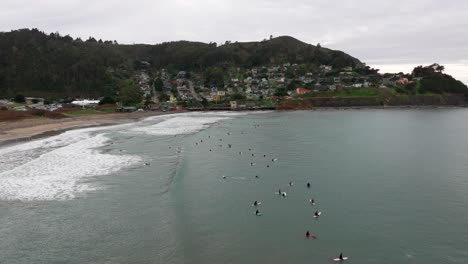 Toma-De-Retroceso-De-Un-Dron-De-Surfistas-Y-Una-Ladera-De-Casas-De-Playa-En-Pacifica,-California