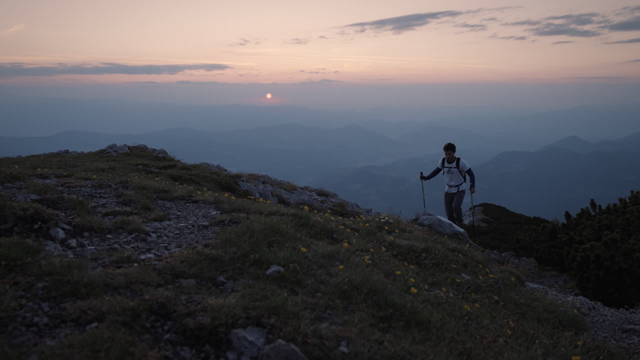 하이킹 폴을 들고 언덕을 오르는 등산객, 탄이 돌아서 아침에 떠오르는 태양을 바라보고 있습니다.