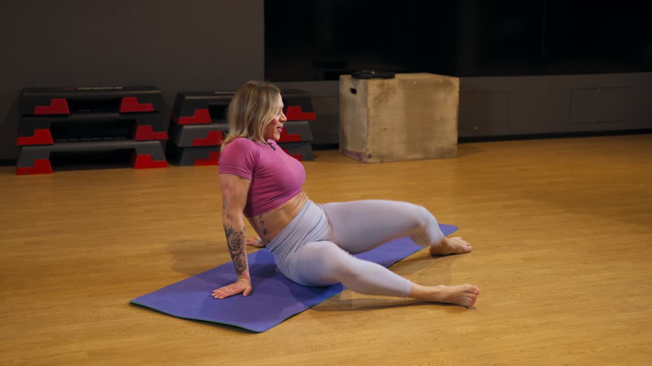 Person stretching on a mat in a gym, twisting hips and knees in flexibility routine to enhance mobility and balance