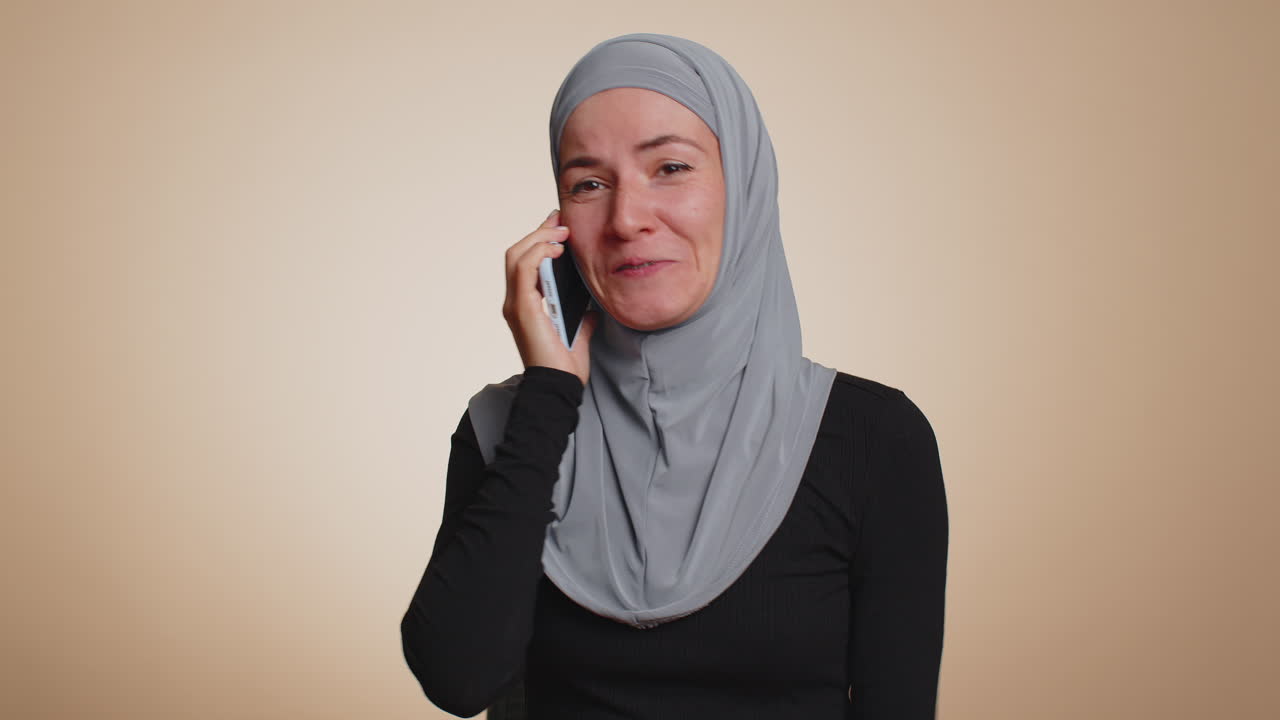 Happy young muslim woman making pleasant mobile phone call conversation with good friend or family