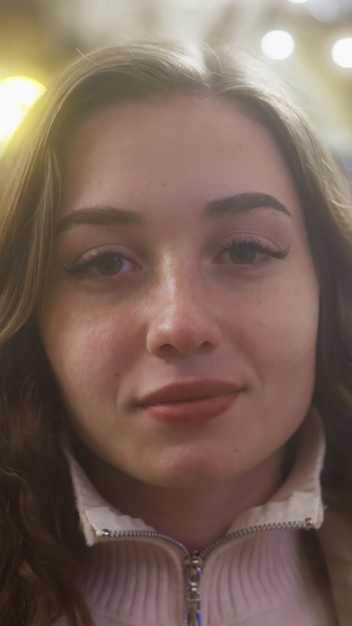 Close-up of cheerful girl smiling as she rests face on hands in cozy cafe, peaceful moment captured with soft lighting creating serene and comforting ambiance