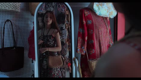 una chica guapa asiática se prueba una bolsa tradicional mirándose al espejo en una tienda en el barrio chino de malasia durante el día