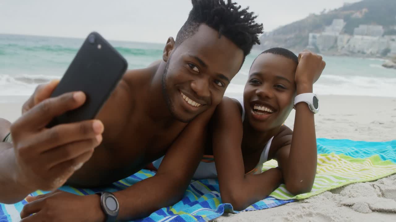 Front view of African american couple taking selfie with mobile phone on the beach 4k