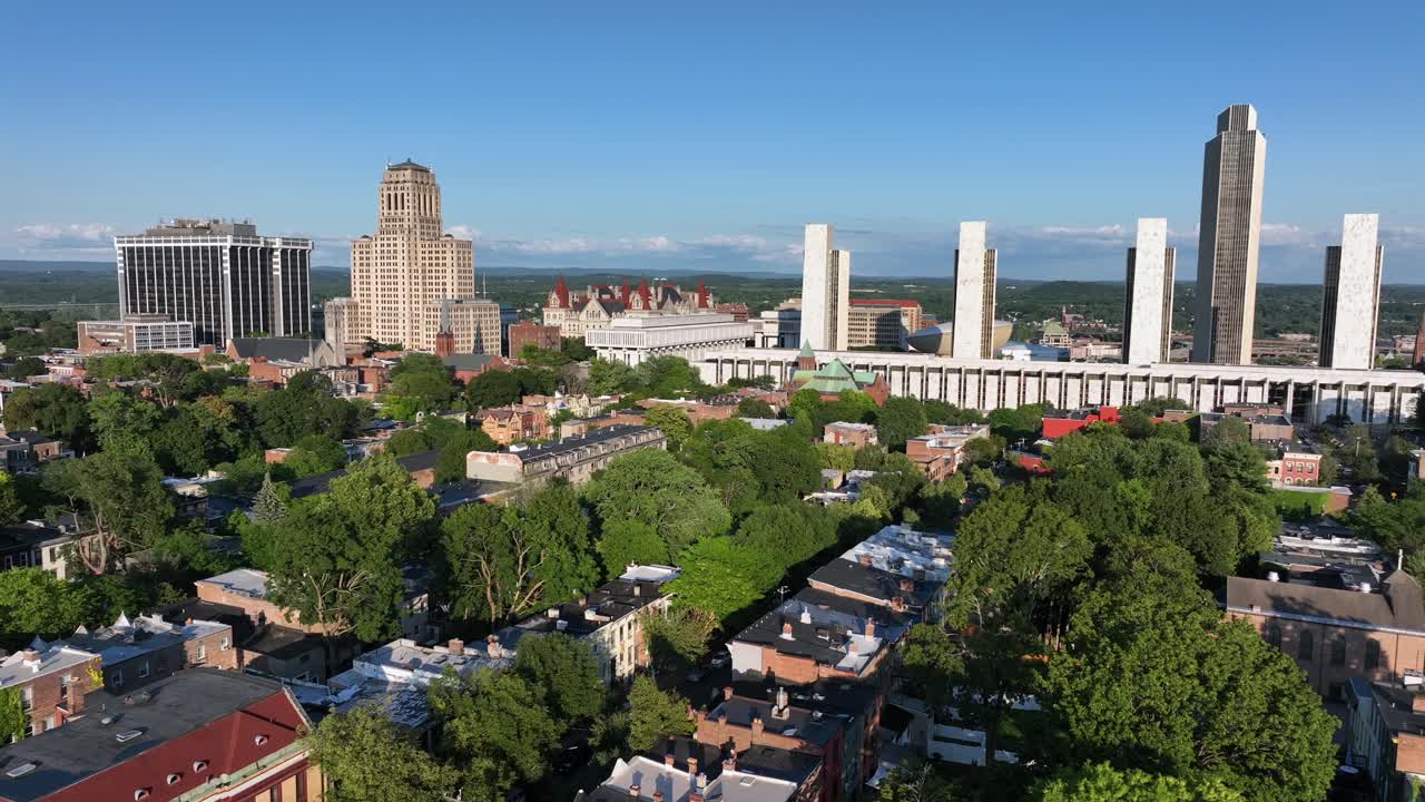 Aerial flight over quiet housing area with two-story homes near downtown of Albany, New York. Sunny day in summer with green trees. Empire State plaza with tower in background