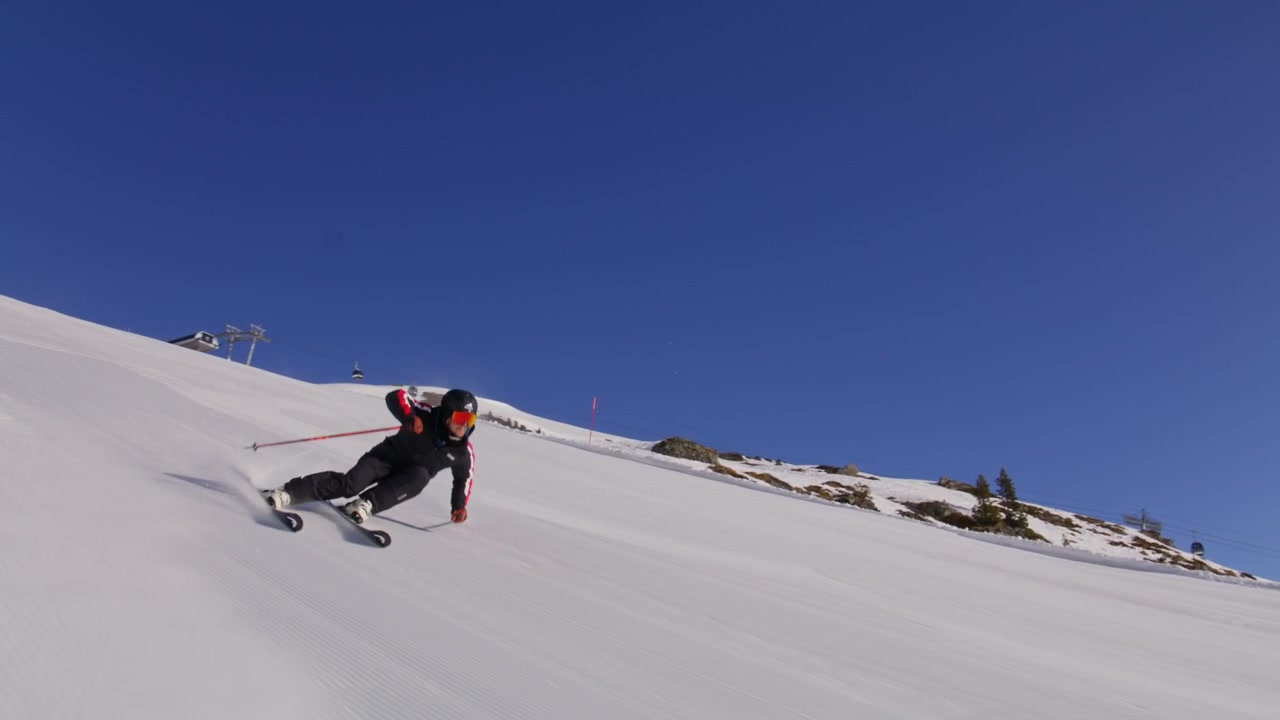 Sciatore che intaglia piste battute ad alta velocità a Nendaz, parte del comprensorio sciistico 4 Vallées nelle Alpi svizzere. Sci alpino d'élite con potenti spruzzi di neve e tecnica di precisione.