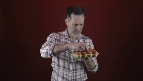 A-middle-aged-man-holding-a-white-egg-from-a-carton-of-brown-eggs