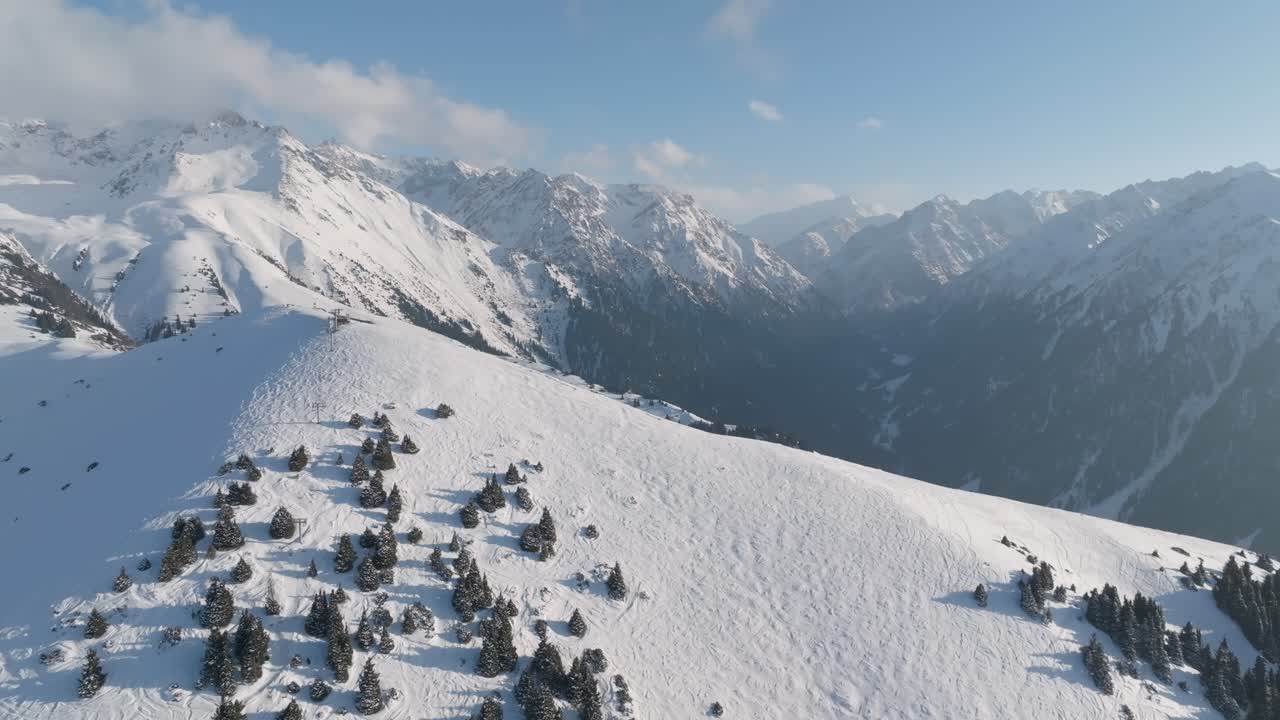 Filmato drone di un crinale montuoso innevato con pini sparsi e cime spettacolari sotto un cielo blu vicino a Karakol, Regione di Issyk-Kul, Kirghizistan