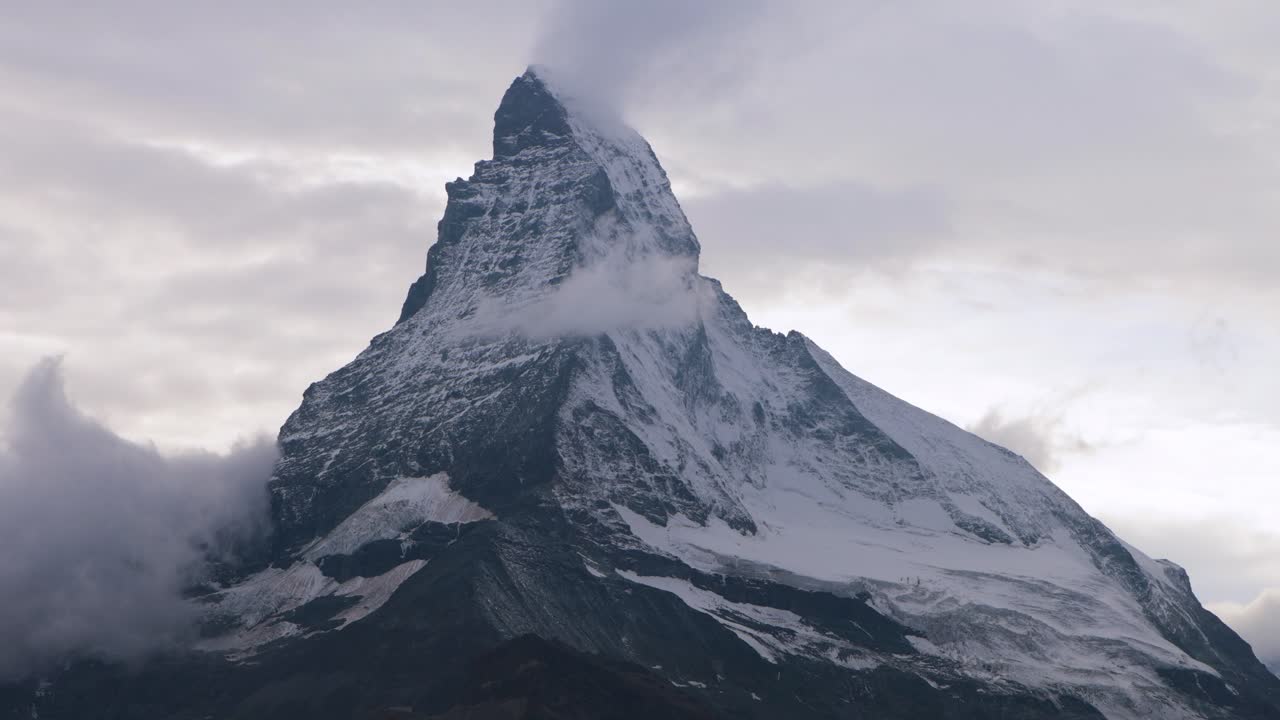 Behold the legendary Matterhorn, one of the world’s most iconic mountains, rising majestically from the heart of the Alps. Its distinctive pyramid shape pierces through a veil of swirling clouds
