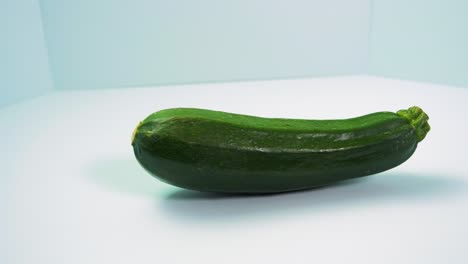 green fresh zucchini squash rotates on a light blue background, healthy food, concept, medium close up shot camera rotate left