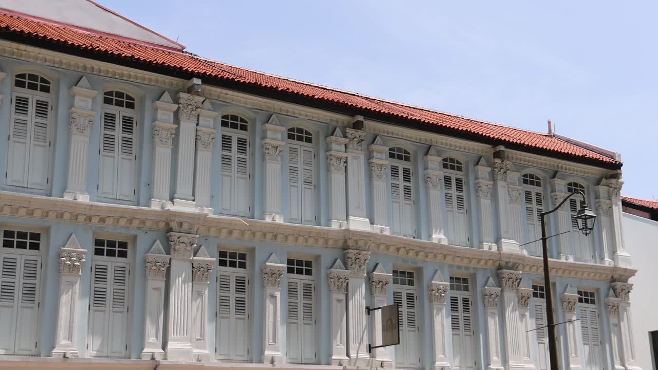 Camera slowly pans across a historic colonial shophouse under bright daylight, revealing architectural details and adjacent buildings on a Singapore street