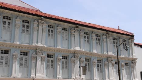 camera slowly pans across a historic colonial shophouse under bright daylight, revealing architectural details and adjacent buildings on a singapore street