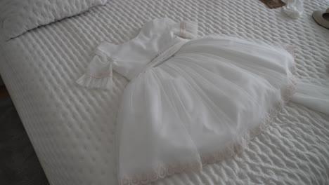 Elegant-white-baby-dress-with-lace-details-laid-out-on-a-textured-bedspread,-ideal-for-special-occasions-like-baptisms-or-christenings