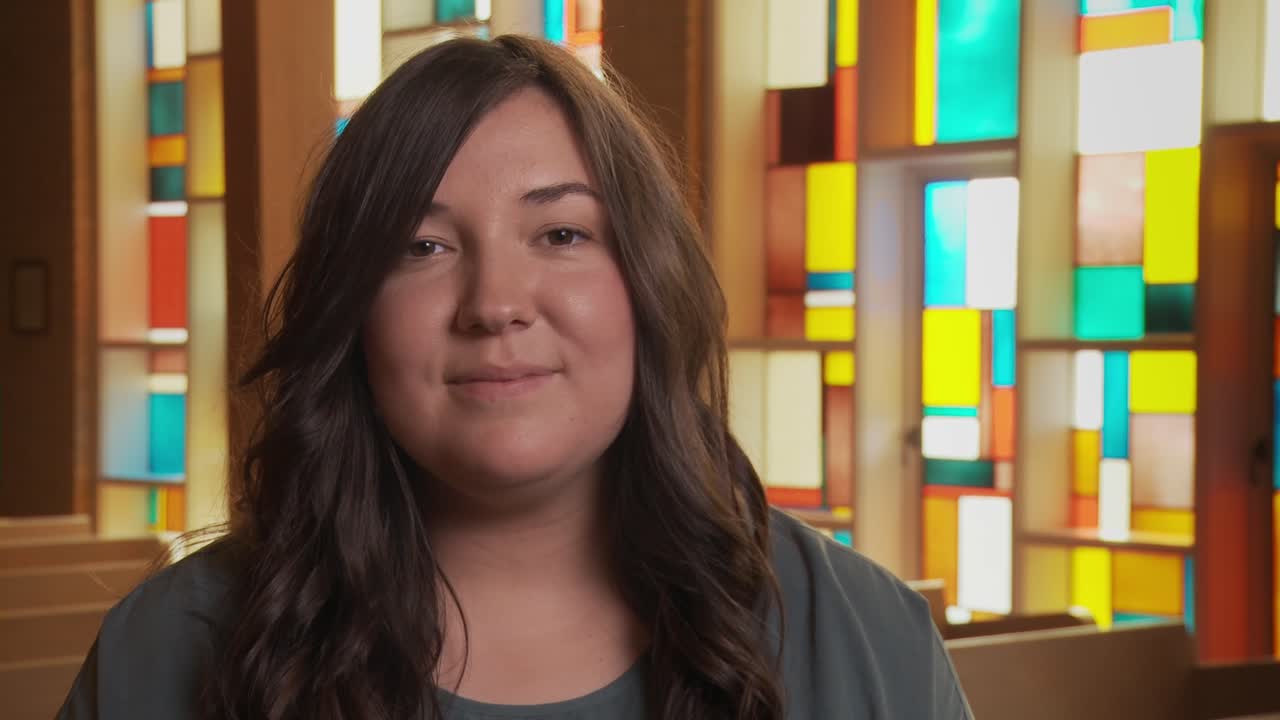 cerca de una mujer étnica bastante joven sonriendo a la cámara dentro de un santuario de la iglesia mientras se sienta en un banco