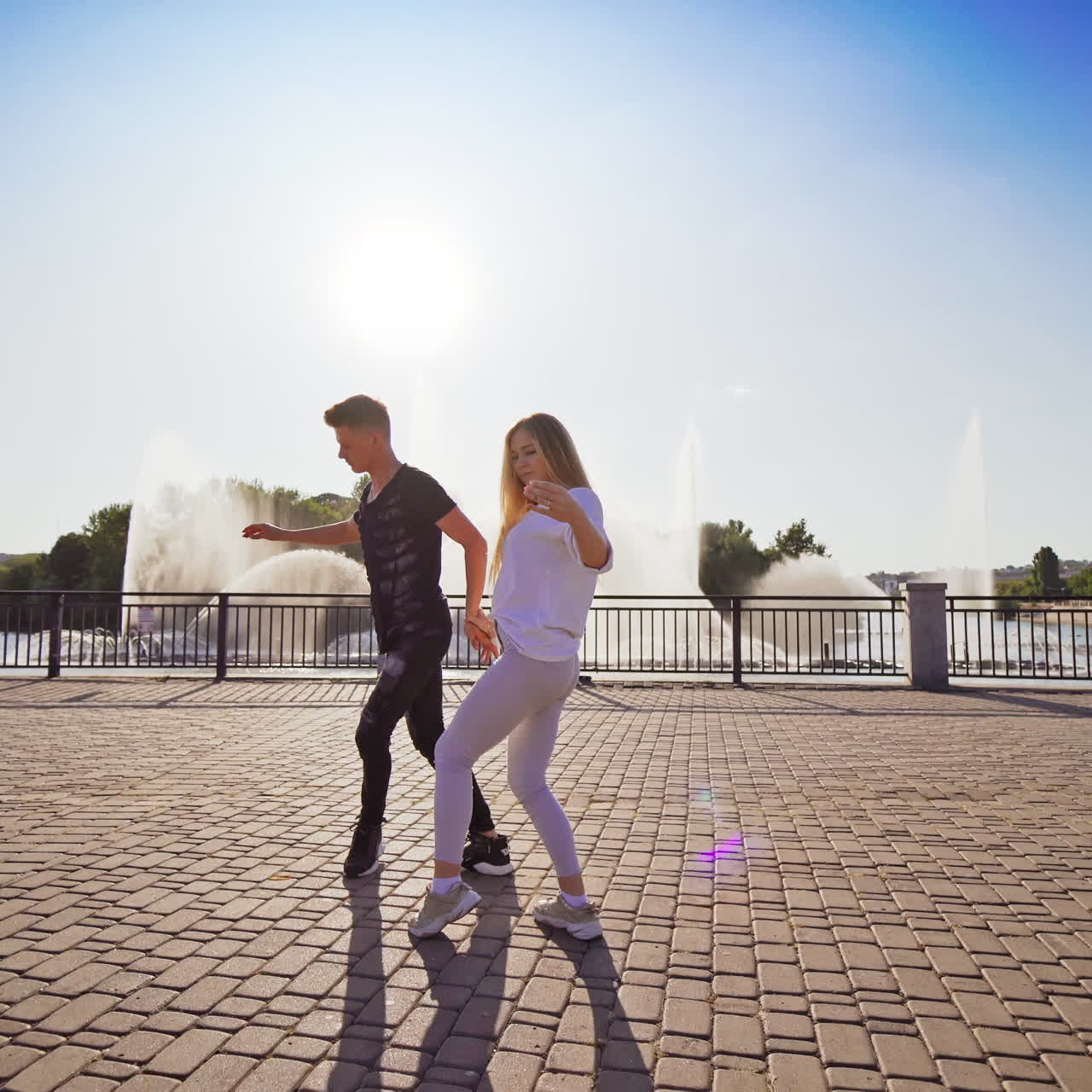 Young dancers moving in tact. Boy and girl dancing together outdoors. Beautiful couple dancing an energetic dance on fountain background.