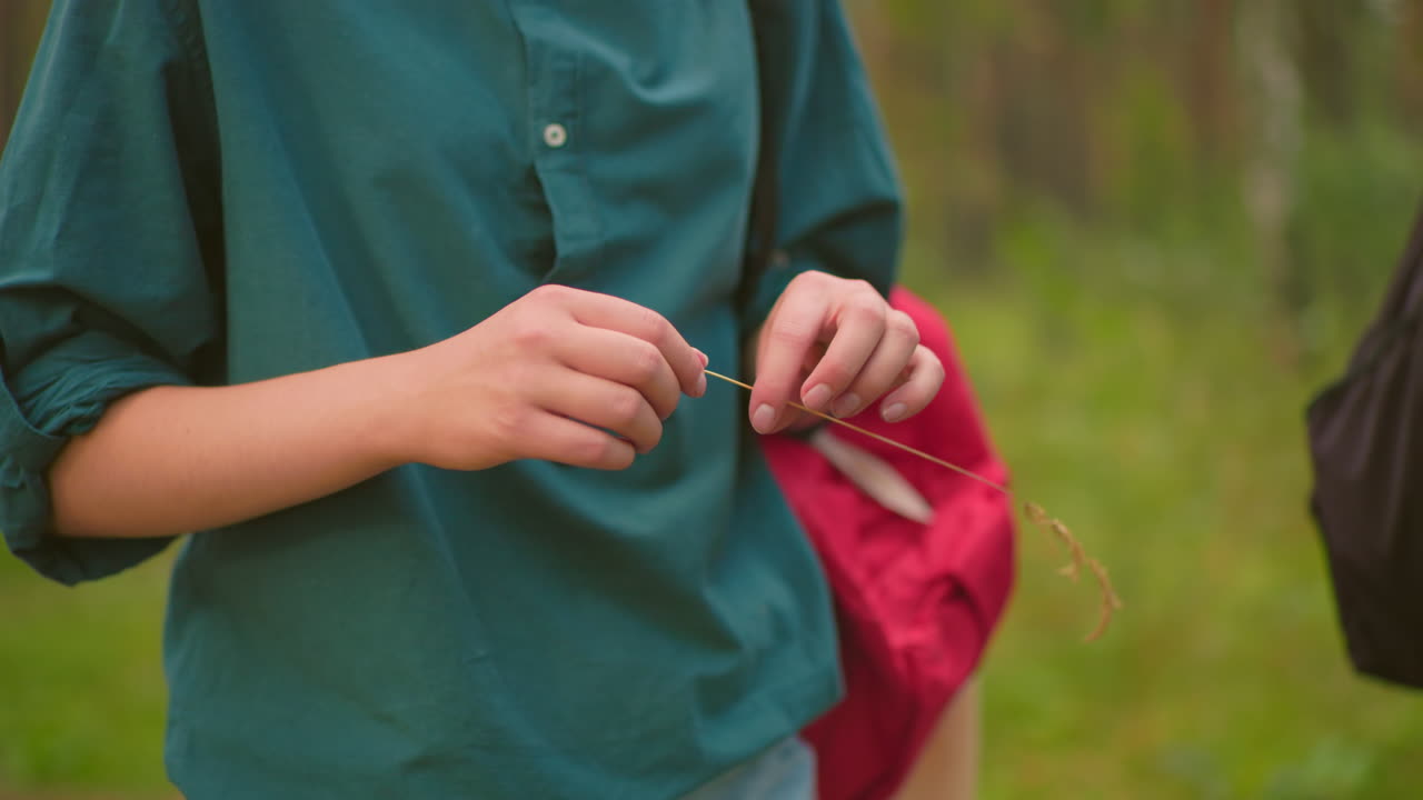 숲길에 있는 한 여자의 클로즈업, 잔디줄을 들고 놀이로 잘라, 그녀는 빨간 배과 함께 초록색 을 입고, 검은 가방을 가진 다른 여자가 부분적으로 보입니다.
