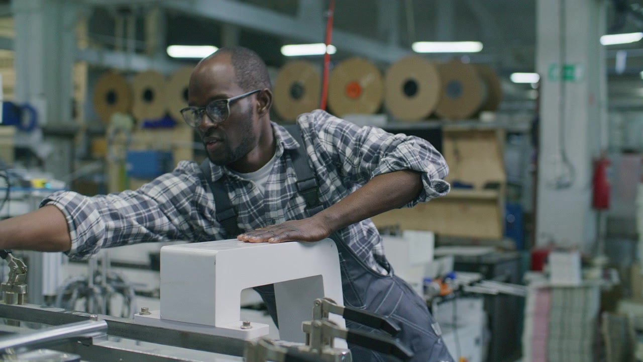 Black Worker Adjusting Clamps on Machinery in Commercial Printing House