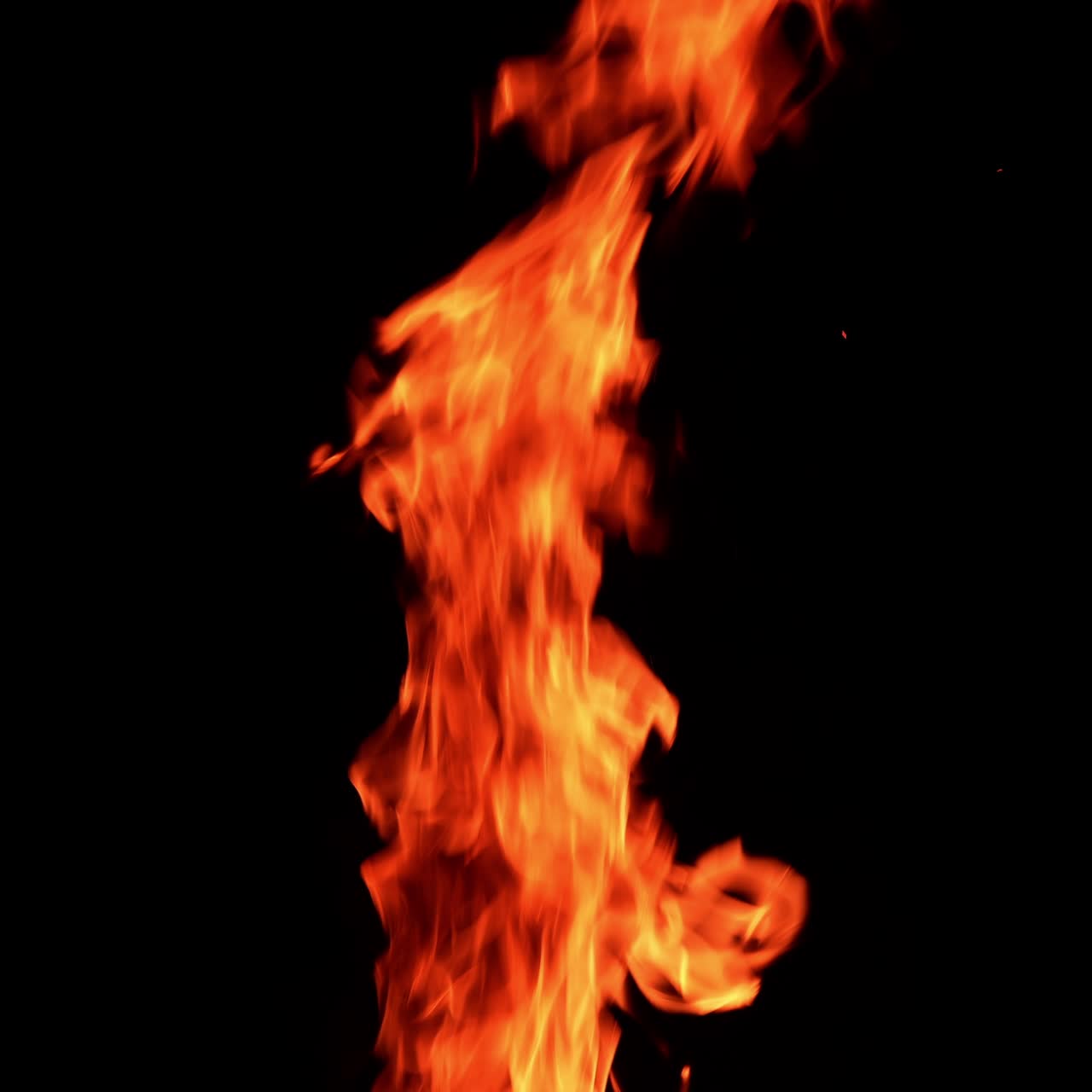 Thin narrow flame burning. Fire going up at the black backdrop. Orange spots flying up