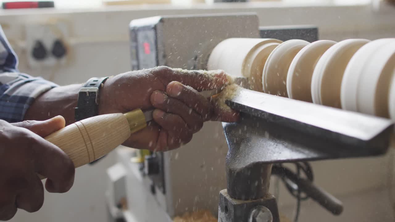 Close up of african american male carpenter hand's turning wood on a lathe at carpentry shop
