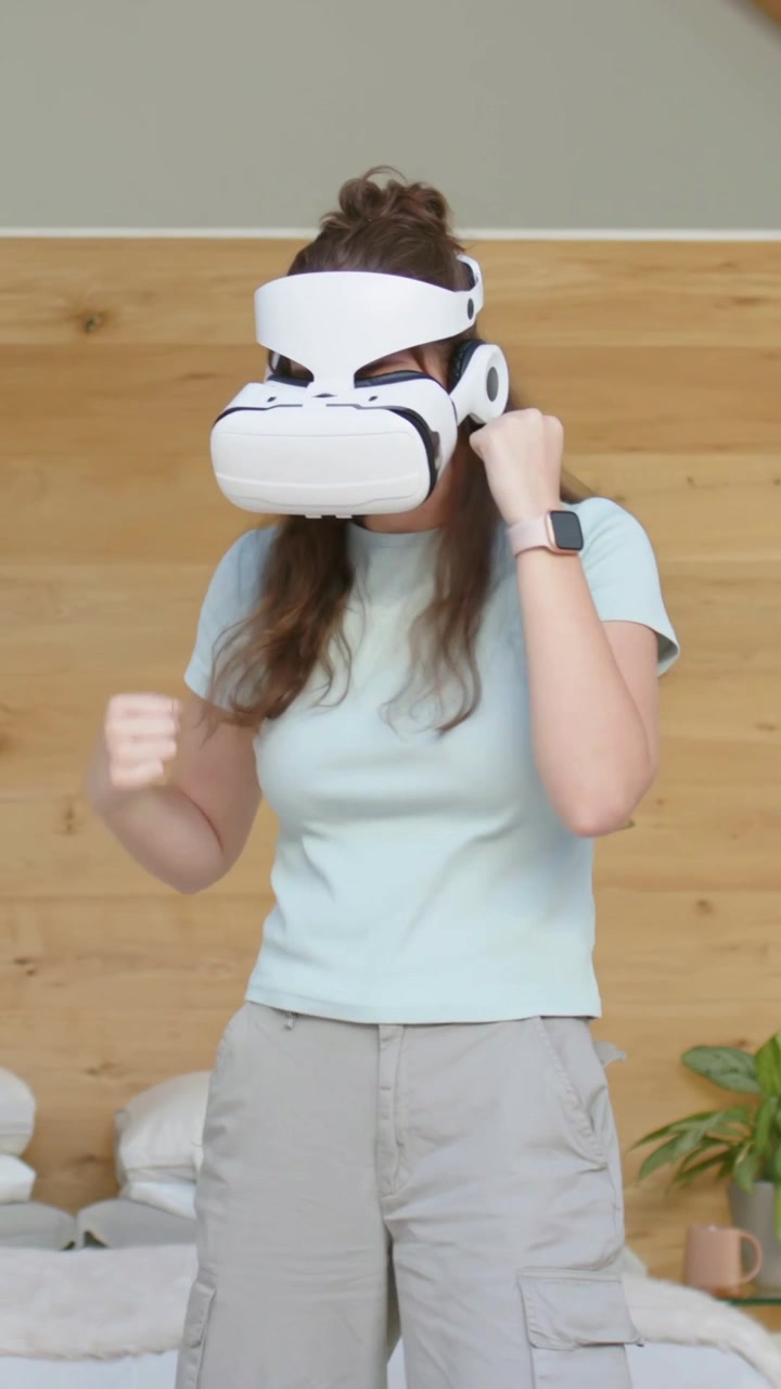 Video verticale: Donna che abbassa il visore VR, fa boxe in un gioco VR a casa, indossando una maglietta color menta.
