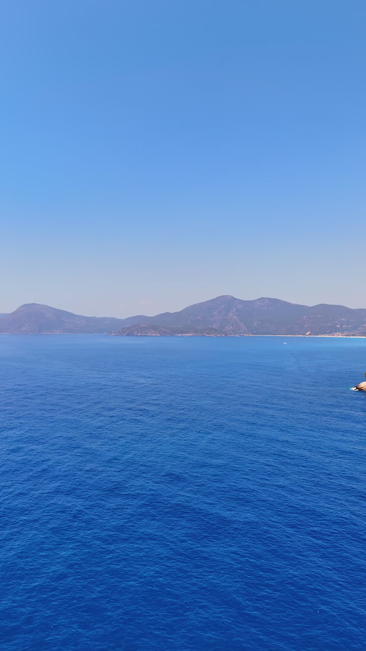 Endless blue ocean meets clear sky. Vast ocean stretches under a clear sky, with distant mountains adding to the serene coastal landscape