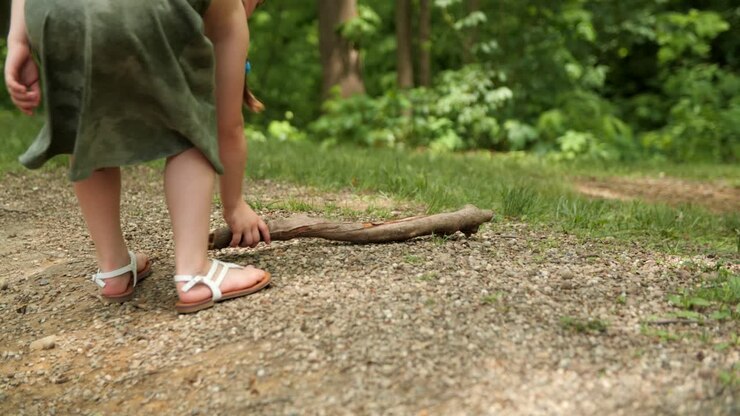 Bambina che raccoglie un bastoncino mentre cammina nel bosco.