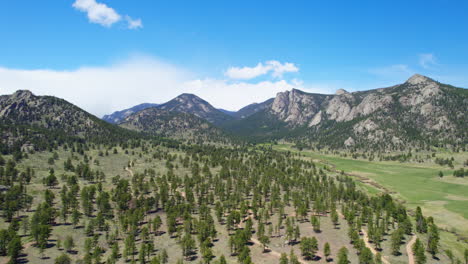 aerial drone shot of beautiful rocky mountain foothills landscape with scenic pine tree forest land and mountain range in the background during warm summertime