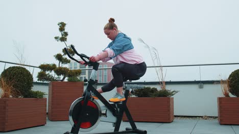 athletic woman riding on spinning stationary bike training routine on house rooftop weight loss