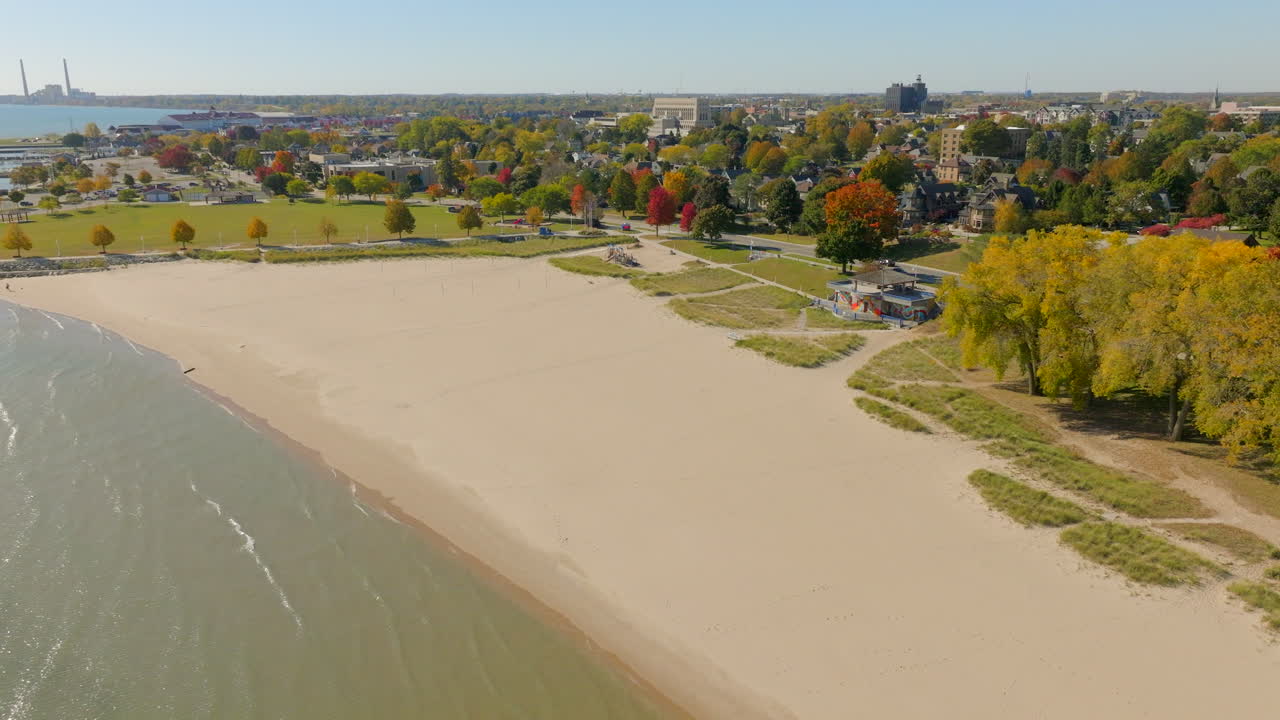 Drone aerial over Lake Michigan turning toward Sheboygan, Wisconsin shoreline and neighborhood with vibrant fall colors on a clear autumn day