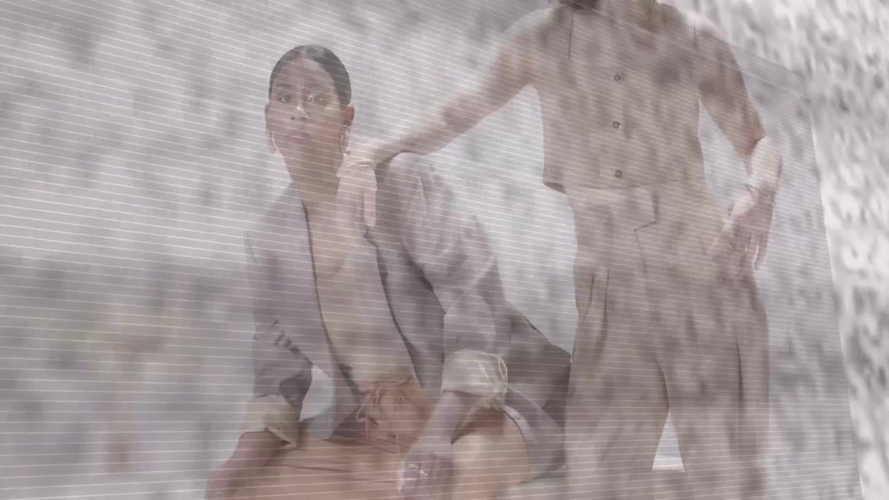 Standing model entering placing hand on seated model causing pose for fashion under grainy veil