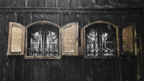 snow falls outside twin iron windows on dark wood panel church in cesky jiretin