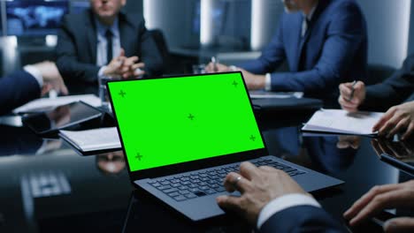 on the table laptop showing green mock-up screen: team of politicians, corporate business leaders and lawyers sitting at the negotiations table in the conference room, trying to come to an agreement.