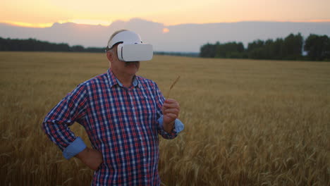 An-elderly-farm-uses-a-VR-helmet-while-standing-in-a-field-at-sunset.-Use-gestures-for-virtual-reality-in-agriculture.