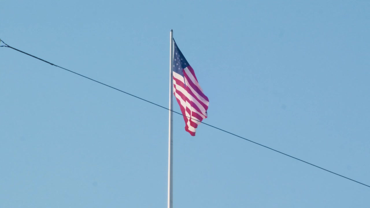 Bendera Amerika berkibar dengan latar langit biru cerah di Los Angeles, pengambilan gambar statis siang hari.