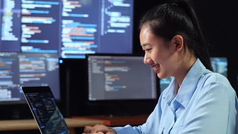 close up side view of asian female programmer writing code by a laptop using multiple monitors showing database on terminal window desktops in the office