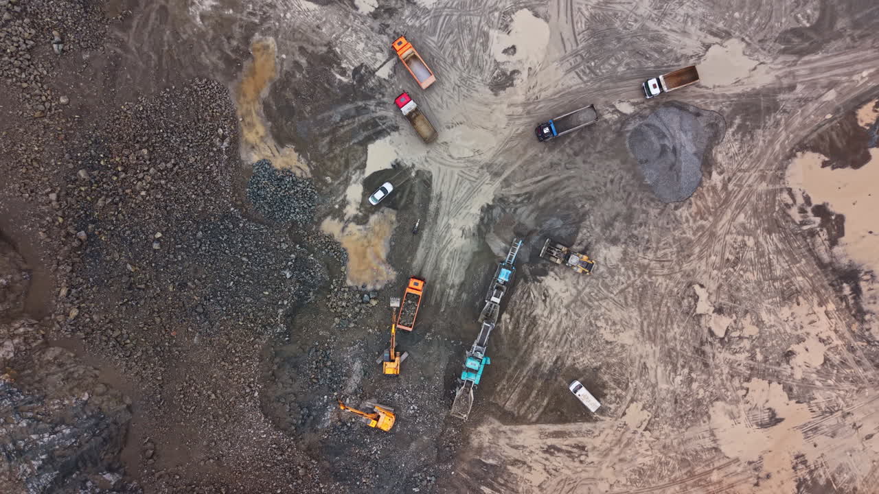 Granite quarry site with heavy machinery, trucks, and excavation activities taking place on a cloudy day in a remote location
