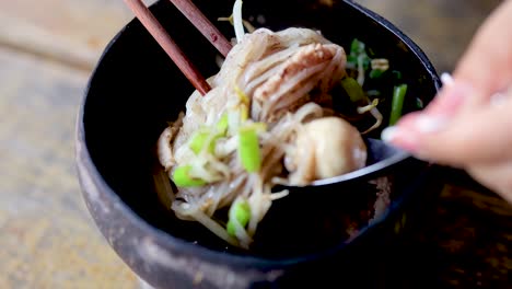 person eating noodles with chopsticks and spoon