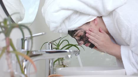 Caucasian-woman-in-bathrobe-with-towel-on-head-cleansing-face-in-bathroom,-slow-motion