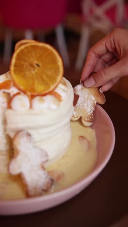 woman placing cookies on a layered dessert with orange slices and custard sauce