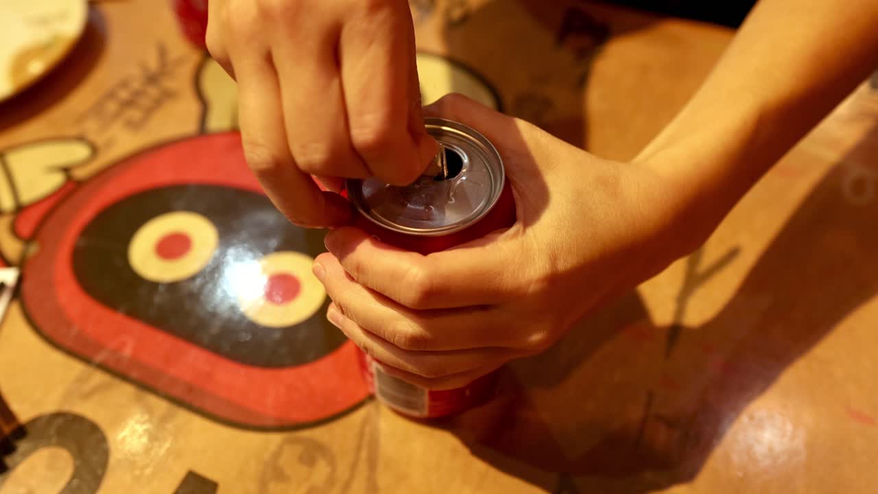 рука открывает банку колы на столе.