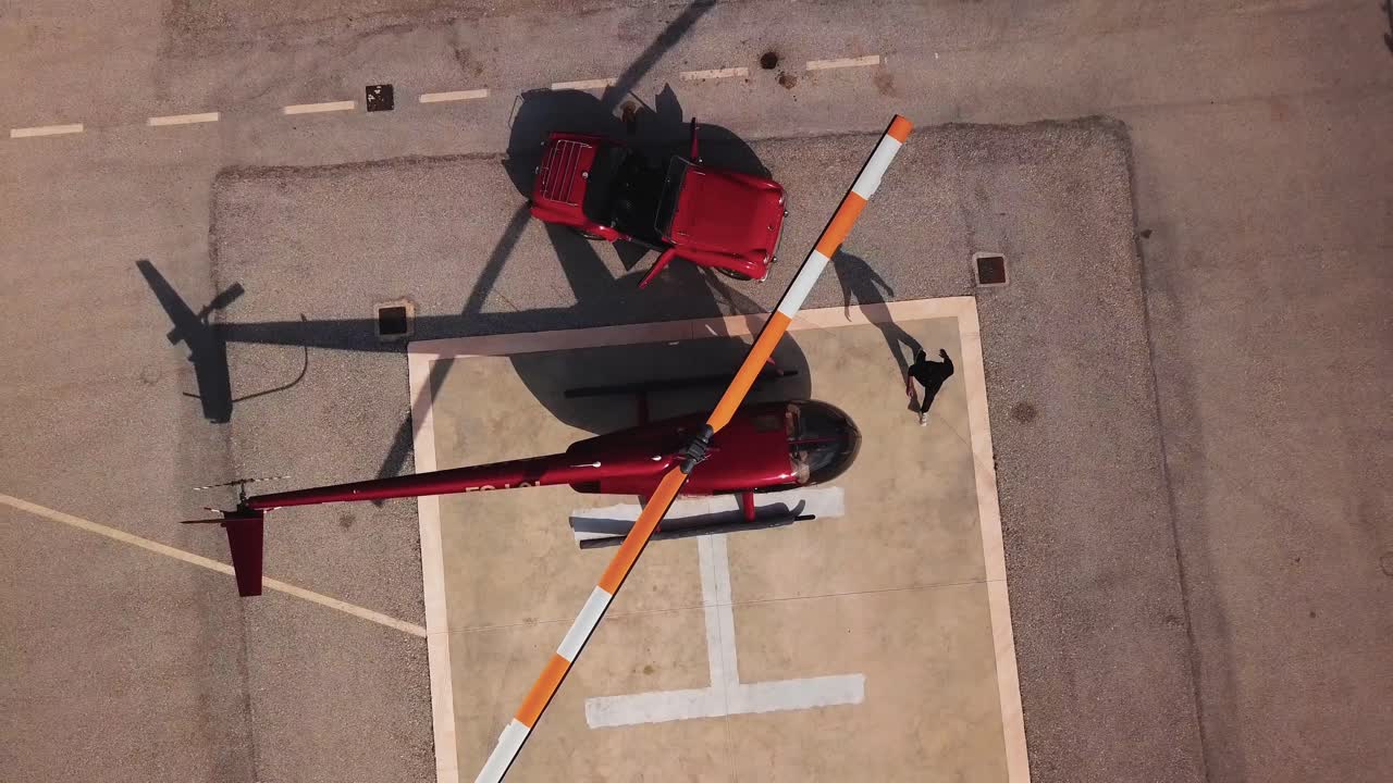 밝고 화창한 날 스페인 베니돔 도시의 헬리패드에 주차된 두 명의 젊은 남자 친구가 빨간색 카브리올레 자동차에서 내리고 헬리콥터에 들어가는 조감도