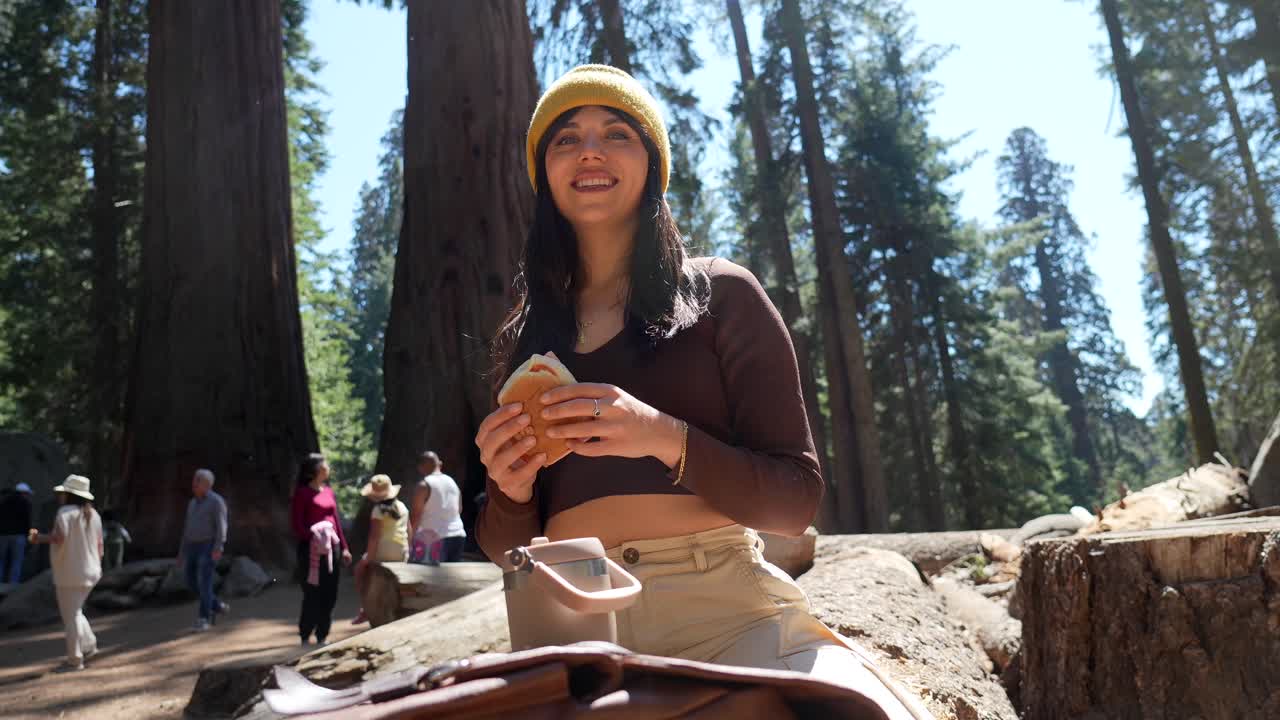 Giovane donna felice che mangia un panino in una foresta di sequoie giganti