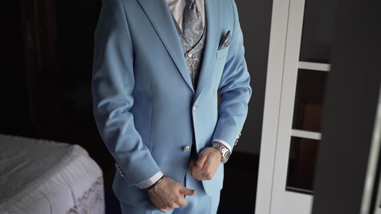 Groom buttoning a tailored light blue suit with elegant details before wedding