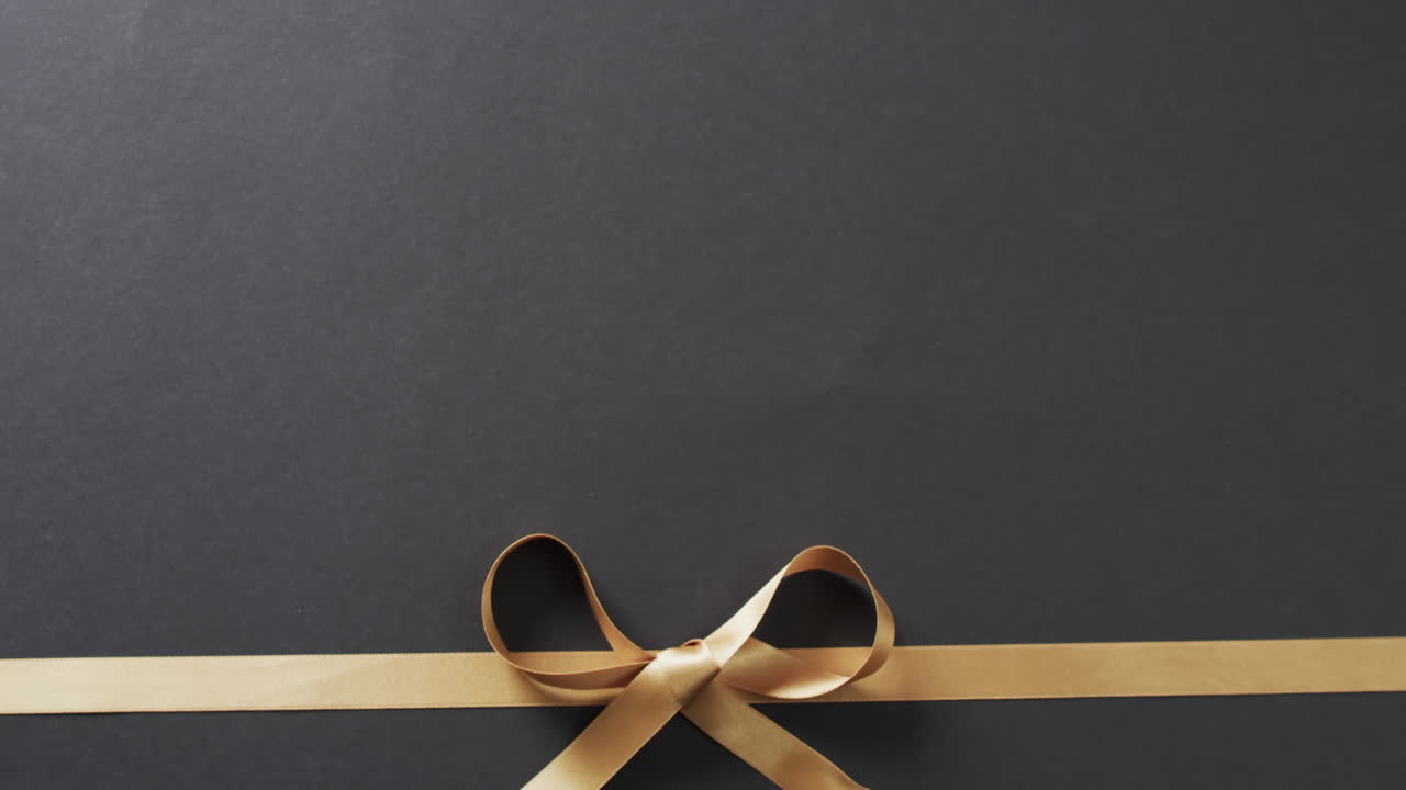 검은색 배경에 복사 공간과 함께 금 선물 리본과 활의 비디오