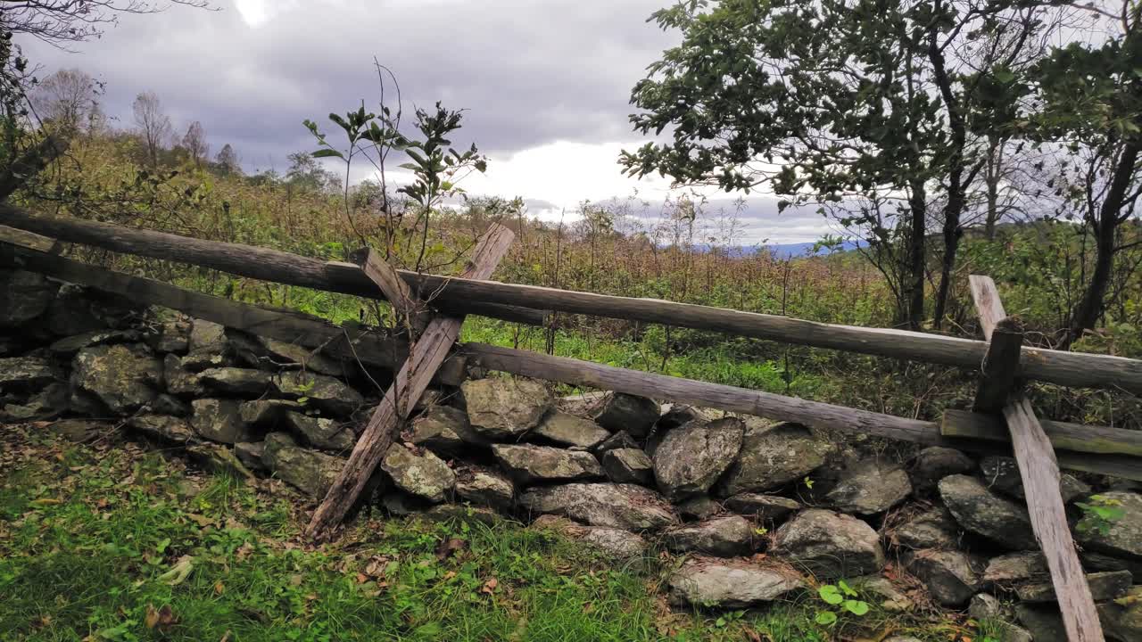 una valla de madera rústica sobre una pared de piedra apilada en seco junto a un campo